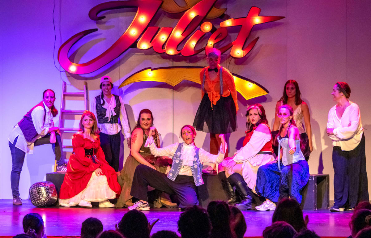 Escena de musical davant un rètol lluminós, amb vestuari d'època i llum magenta