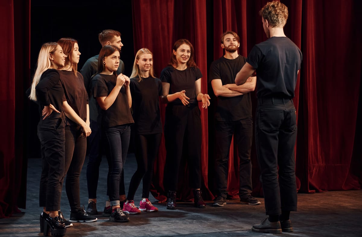 Grup vestit de negre escolta el director dret davant d'un teló vermell