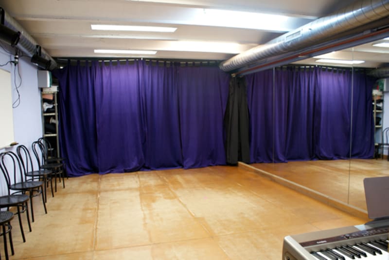 Sala diáfana con cortinas lila, espejo lateral y un teclado en primer término