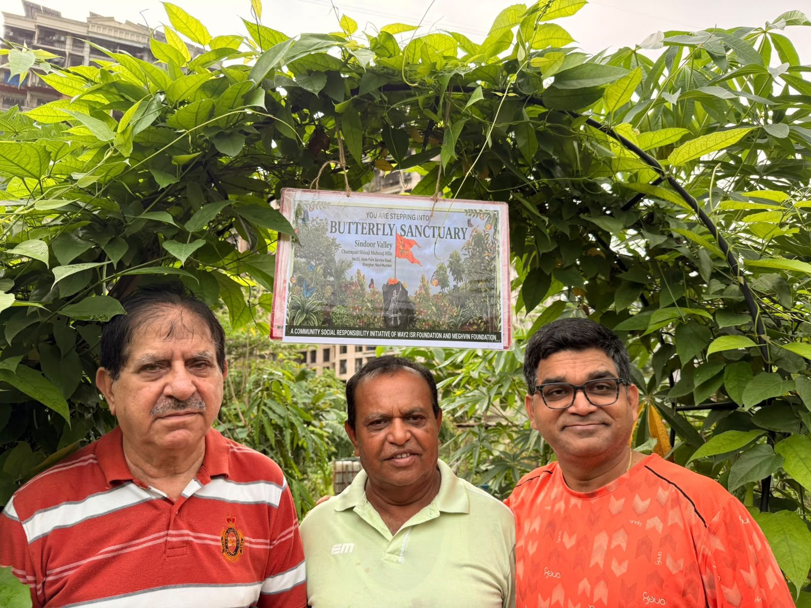 Three volunteers under the Butterfly Sanctuary sign at Sindoor Valley
