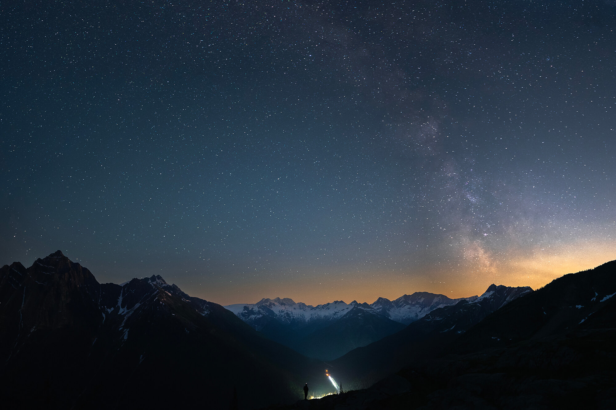 Two hikers looking up at the stars over mountains
