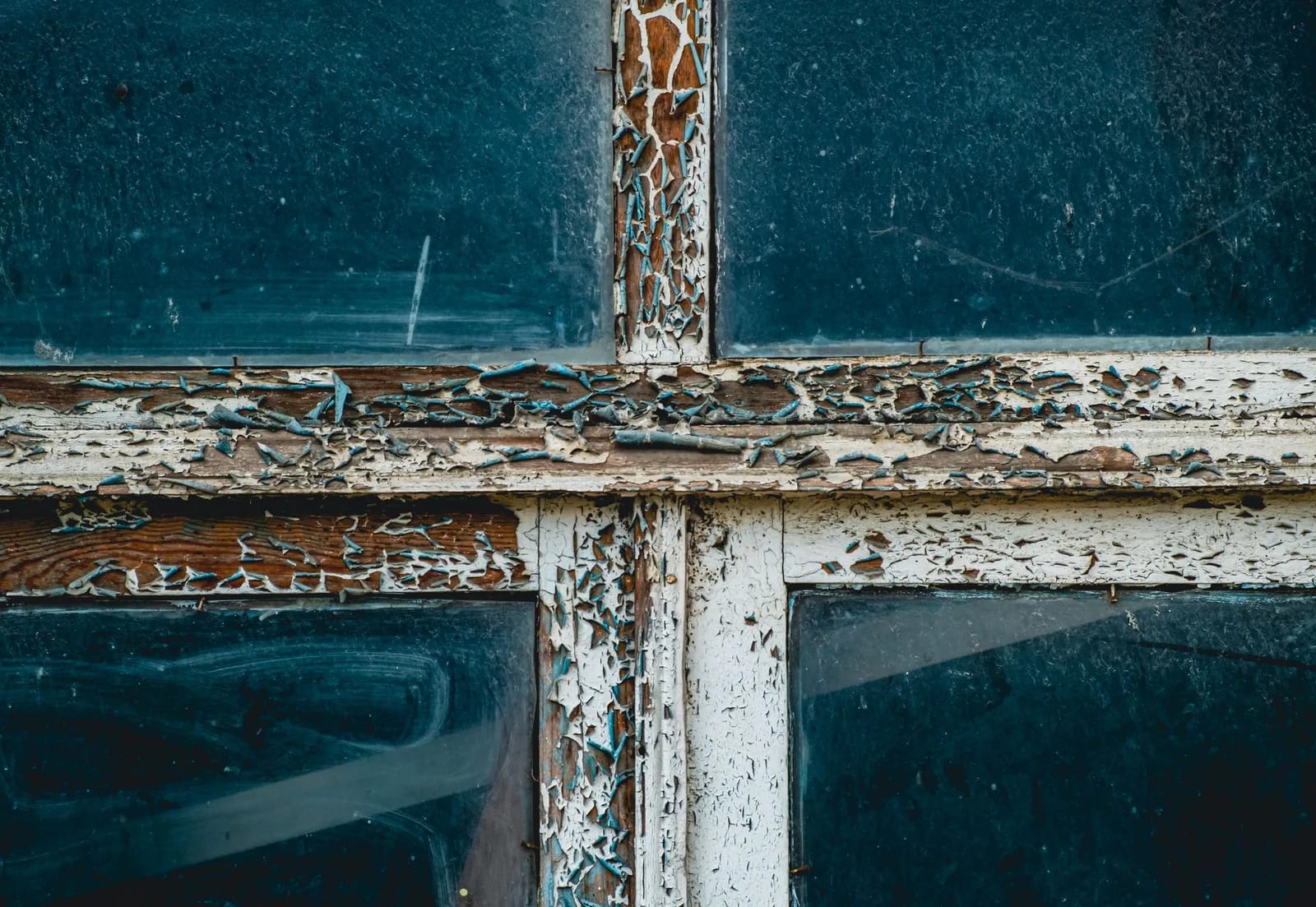 Thickly cracked and peeling white paint on the wooden bars of an old window, with bare wood showing through