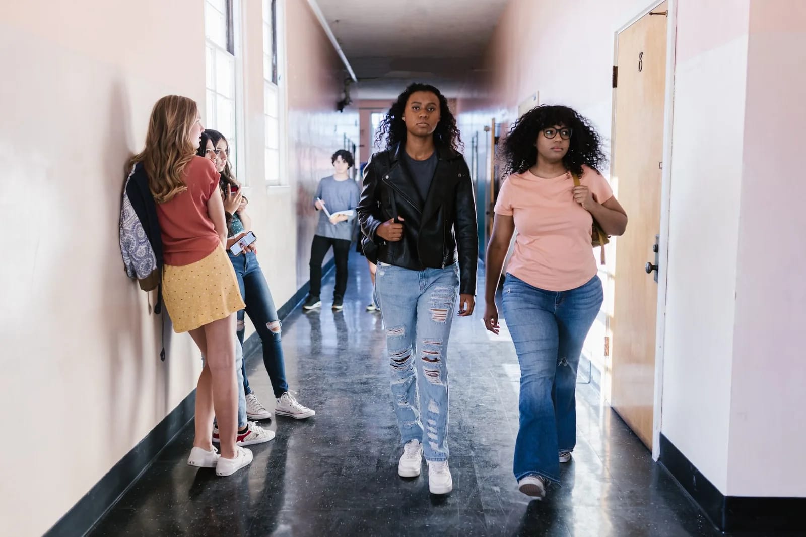 Students walking and talking in a bright school hallway lined with windows