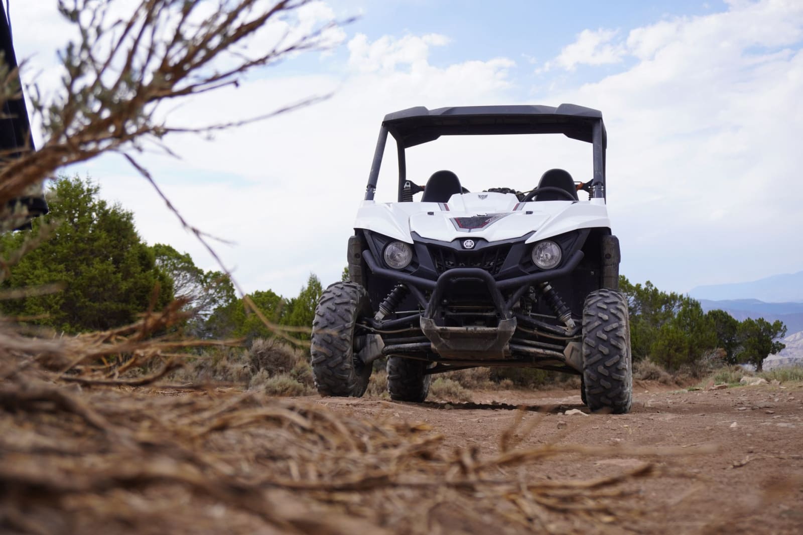 A white side-by-side utility vehicle parked on a dirt track among sagebrush and juniper, with low hills and open sky behind