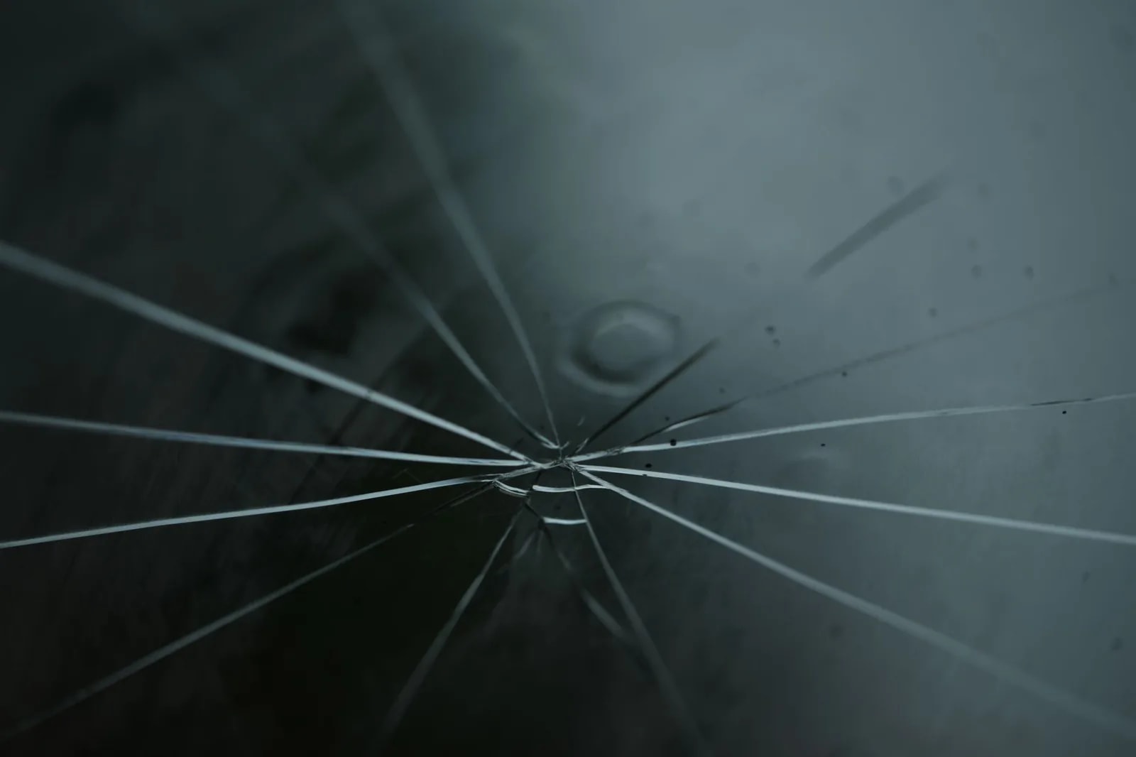 A radial crack spreading outward in fine lines across a pane of dark glass