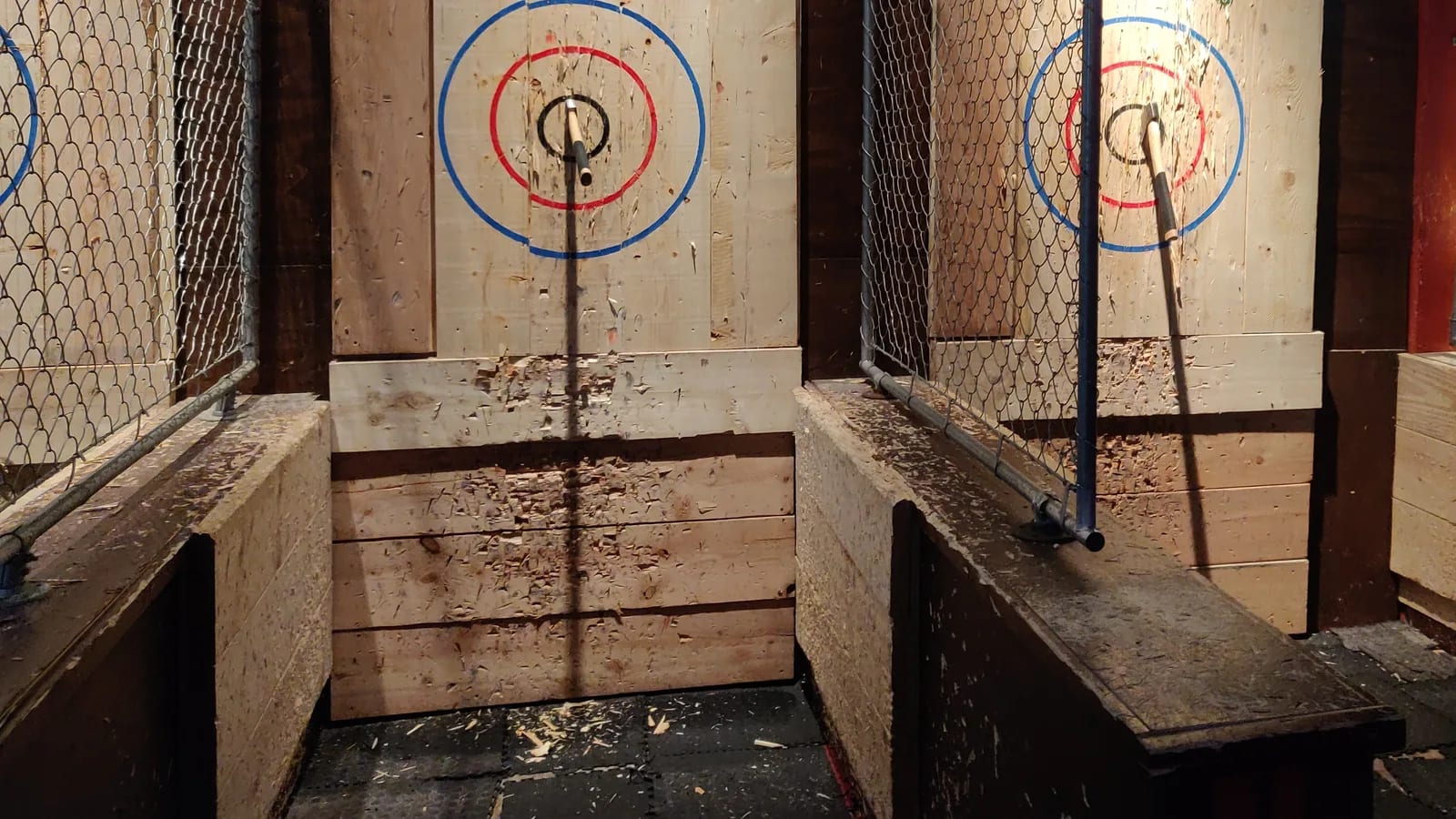 Two caged axe-throwing lanes with bullseye target boards and an axe lodged in the wood