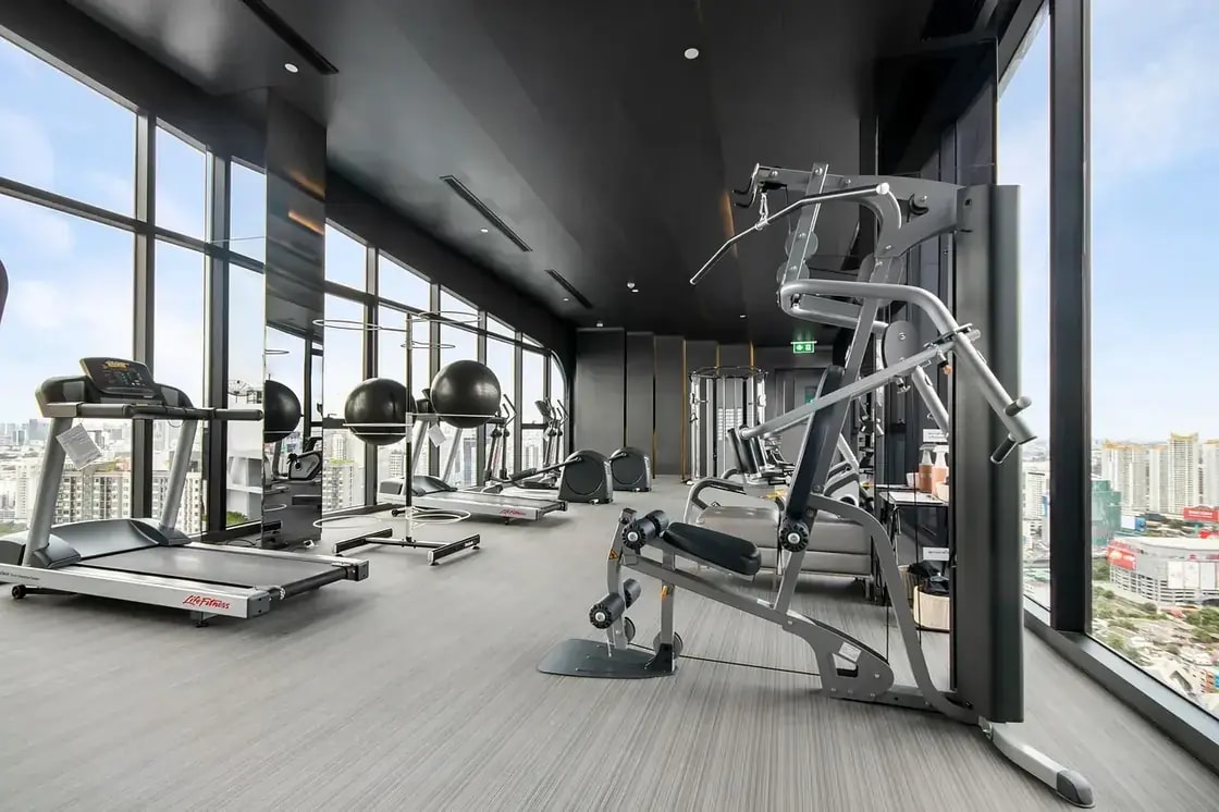Treadmills and weight machines on a gym floor beside floor-to-ceiling windows