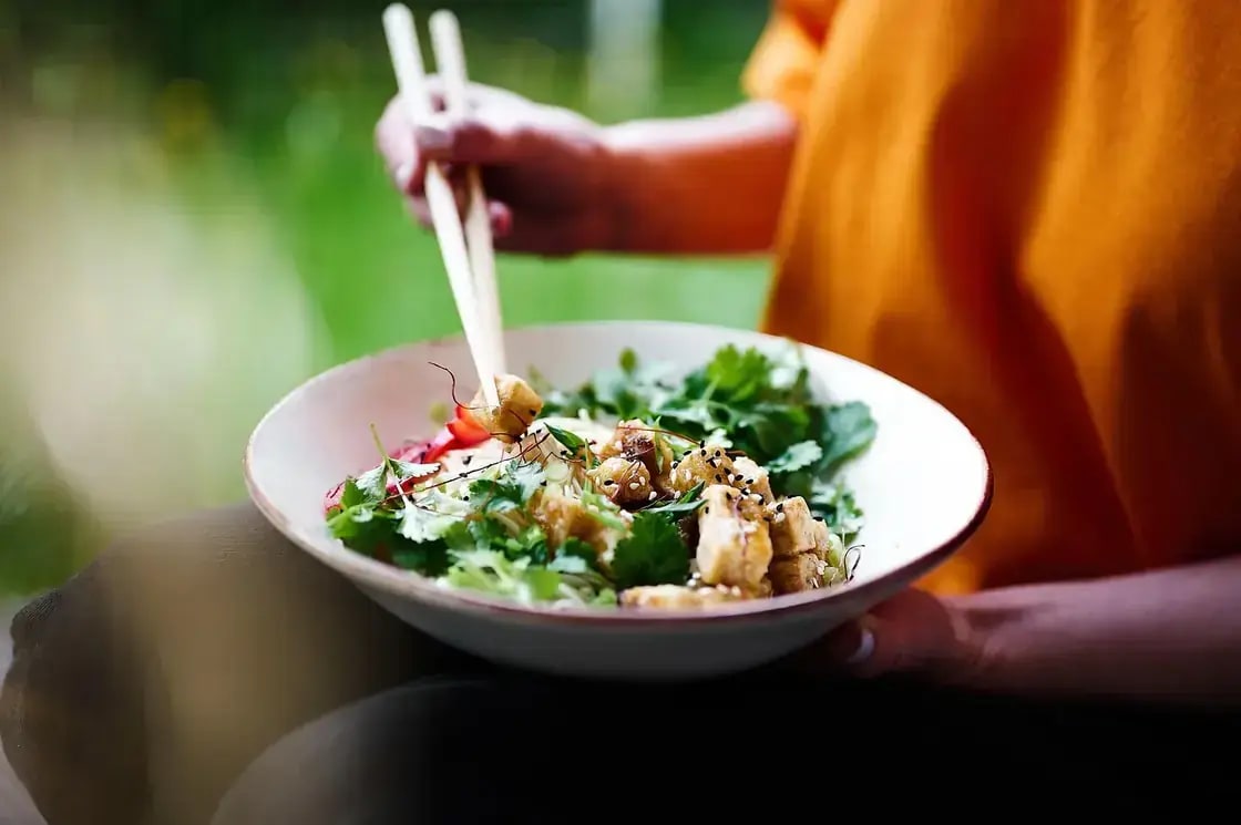 A person holding a bowl of salad with tofu and fresh herbs