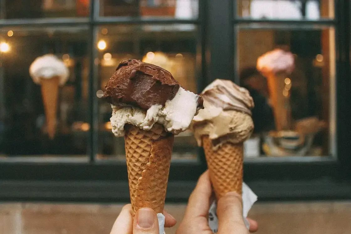 Two ice cream cones held up in front of a shop window