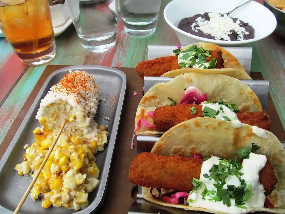 A tray of tacos served with elote and a bowl of beans