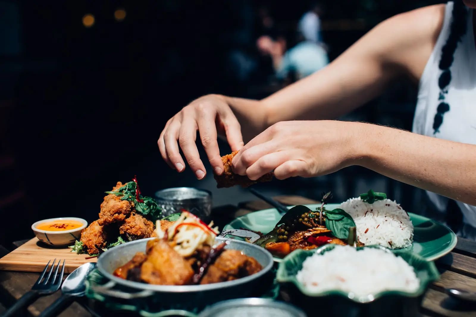 Close-up of a woman's hands enjoying fried chicken and rice outdoors in a restaurant setting
