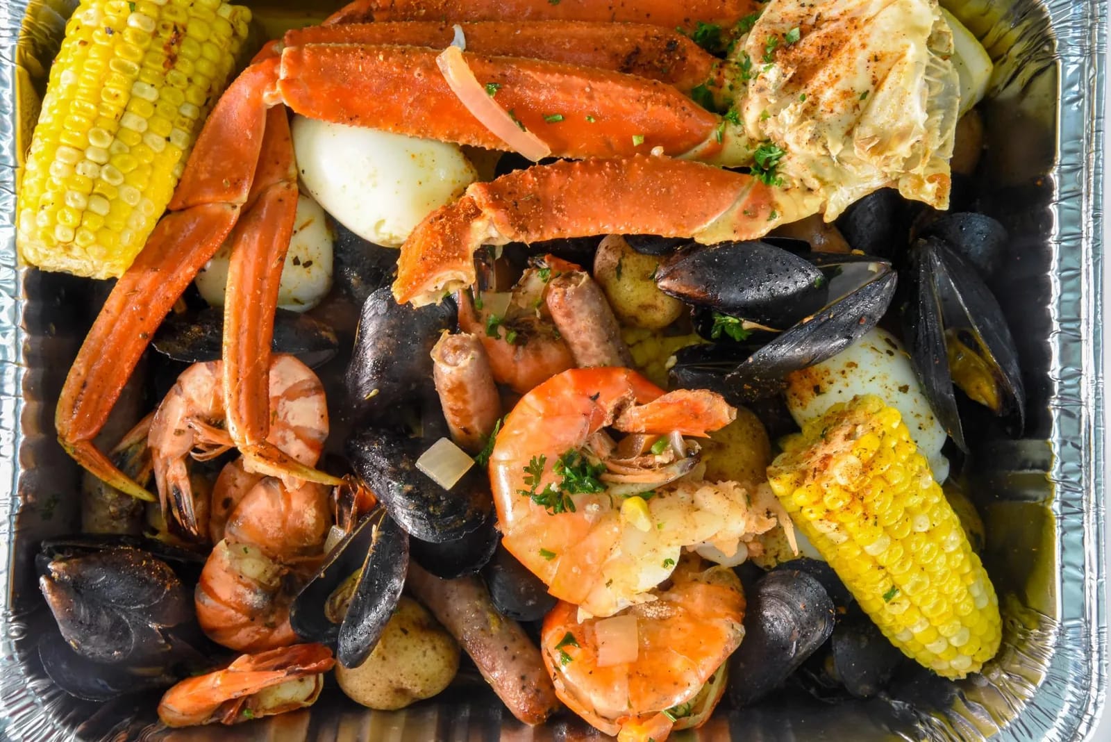A seafood boil of snow crab legs, mussels, shrimp, corn and potatoes in a foil tray