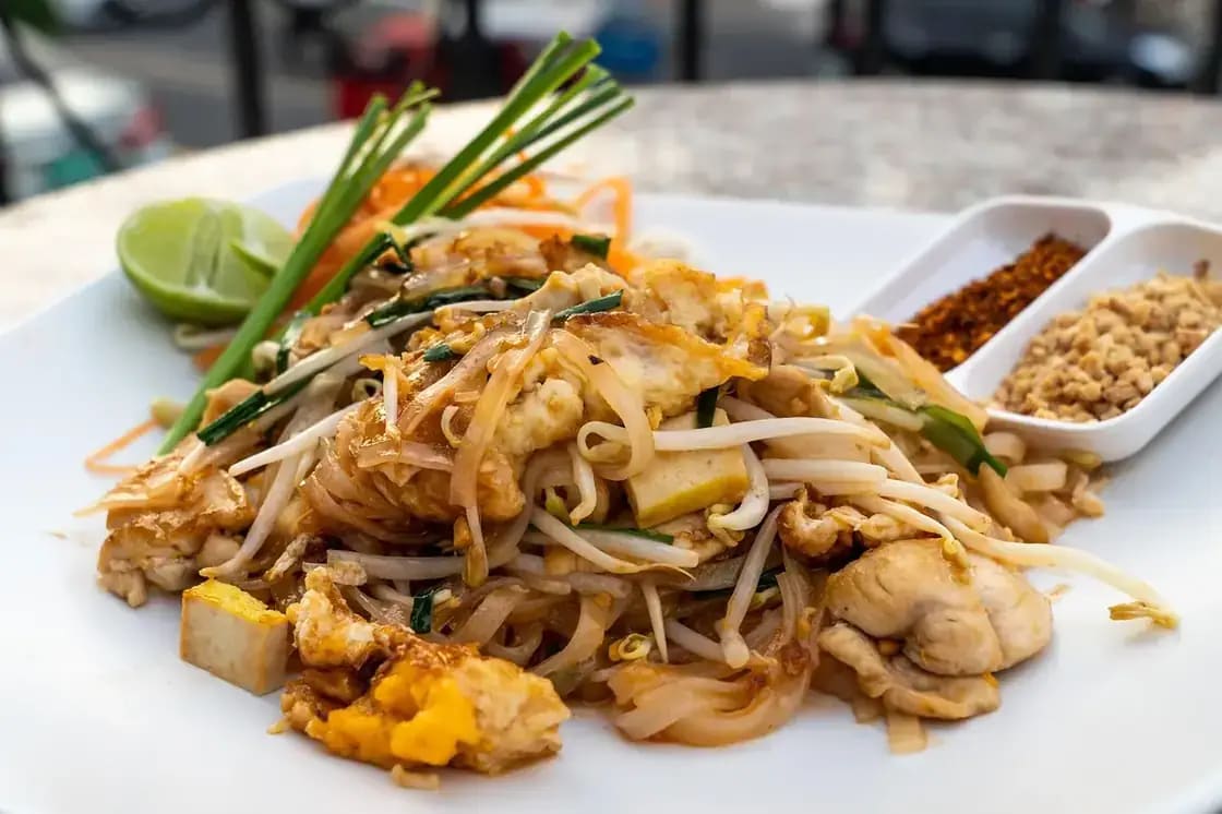 A plate of pad thai with bean sprouts, lime and crushed peanuts