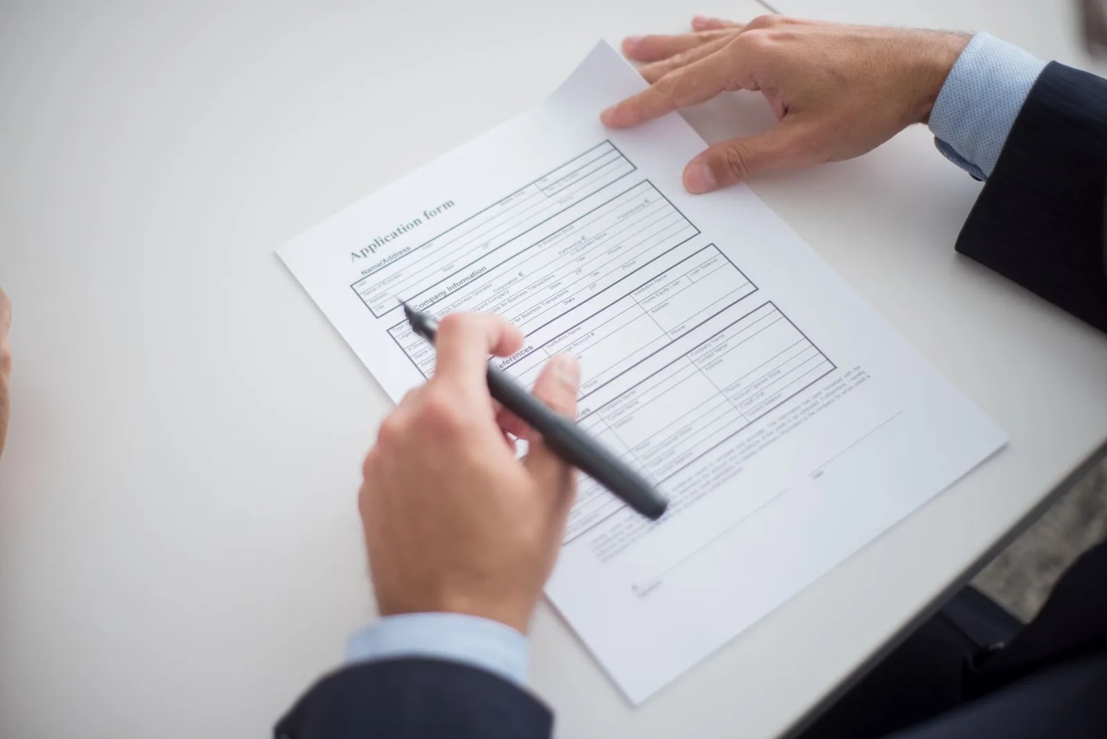 A person filling in a printed application form with a pen, the form's company information and references sections visible
