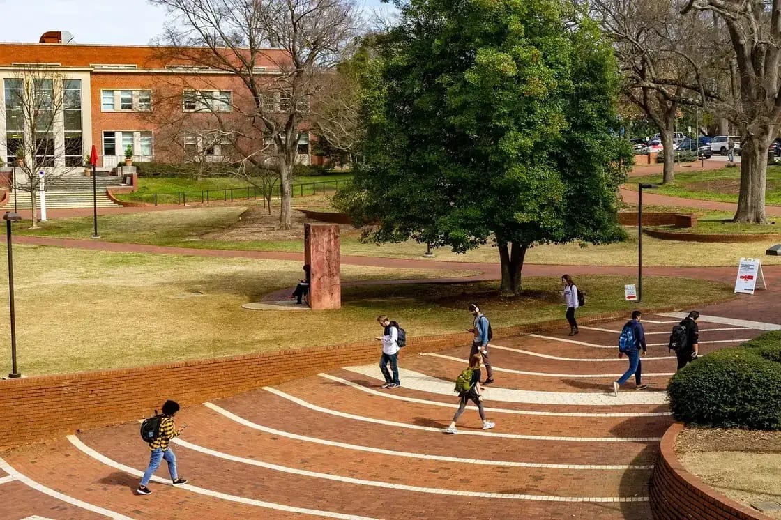 Students crossing a brick campus plaza between academic buildings