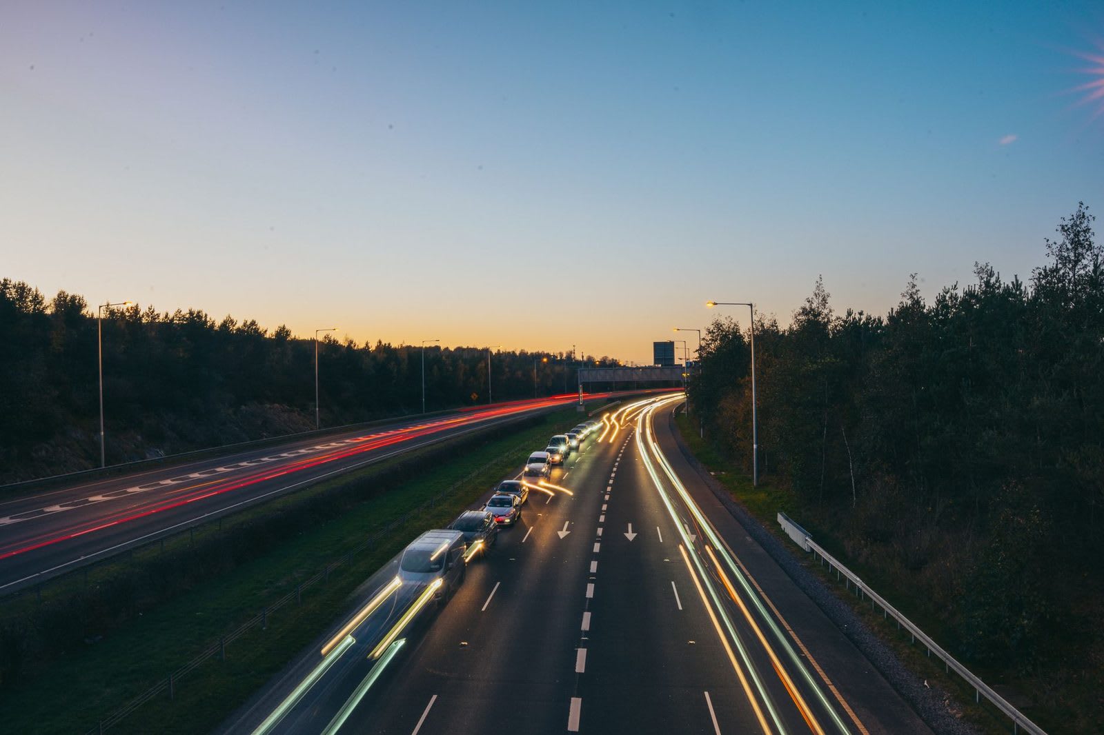 Long-exposure light trails from traffic curving along a divided highway at dusk