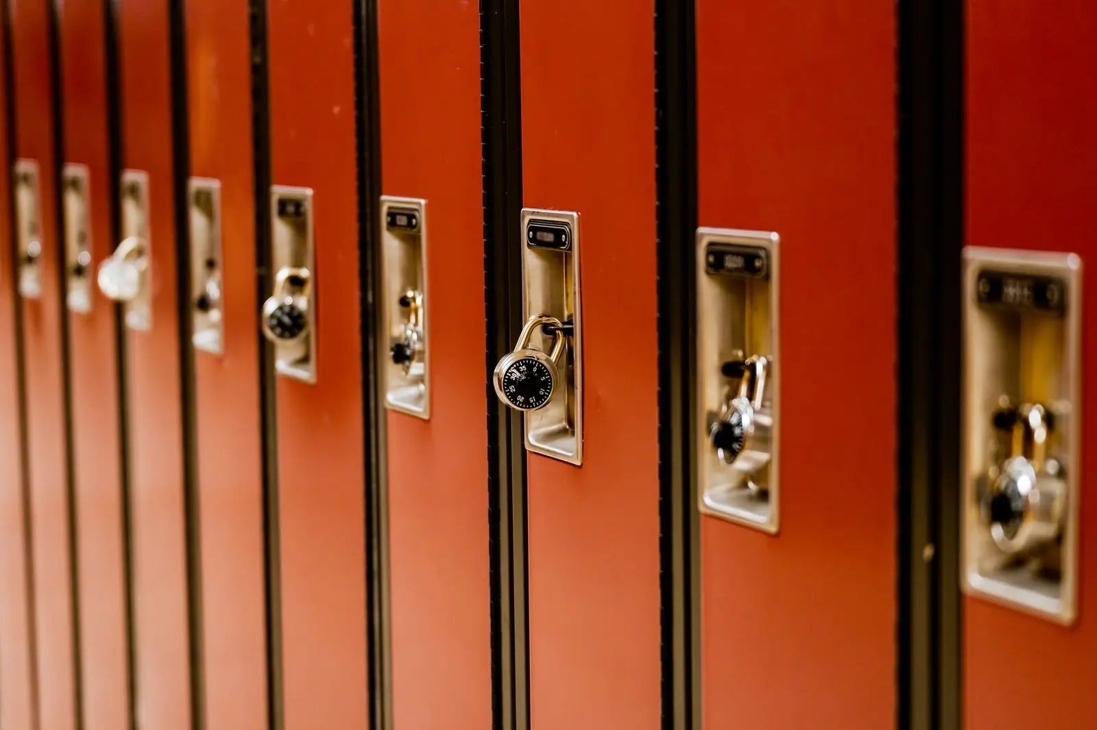 A row of red school lockers with recessed latch plates, one fitted with a combination padlock