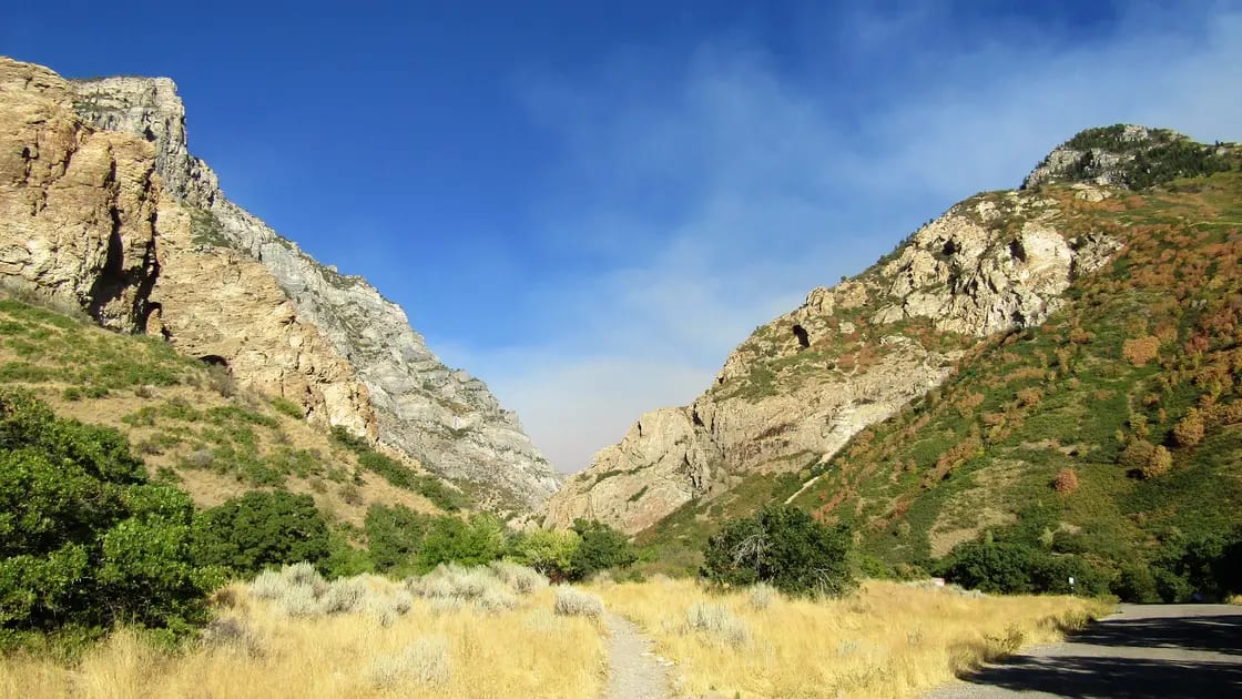 A wide gravel trail running up Rock Canyon in Provo, Utah, between steep rock canyon walls with scrub oak and green brush along both sides
