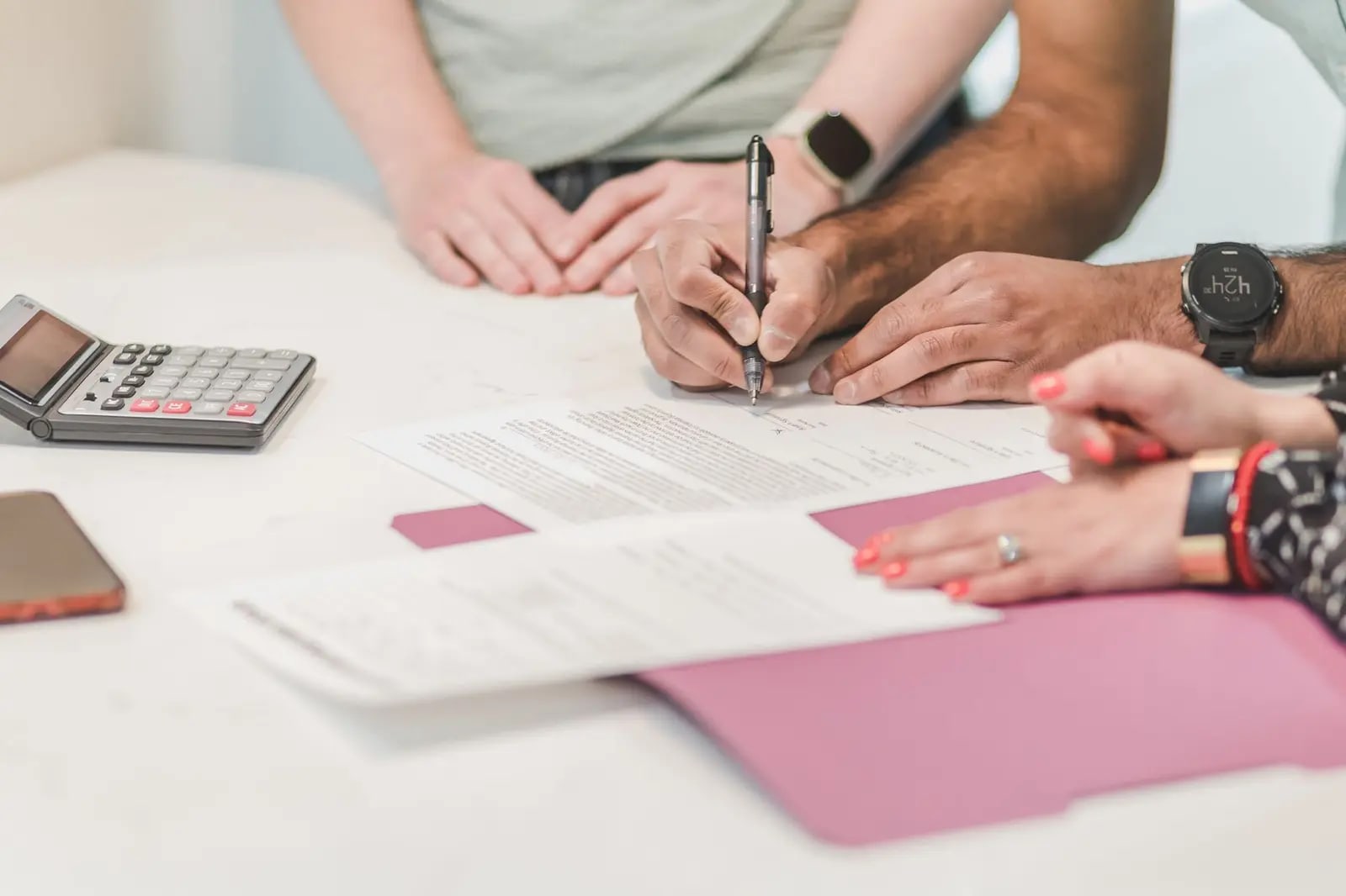 Two people signing paperwork at a white table beside a calculator and a folder