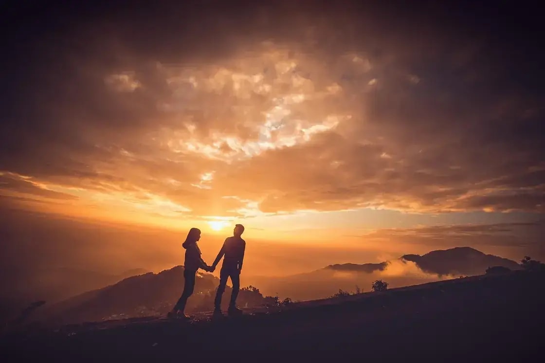 A couple silhouetted against the sunset on a mountain ridge