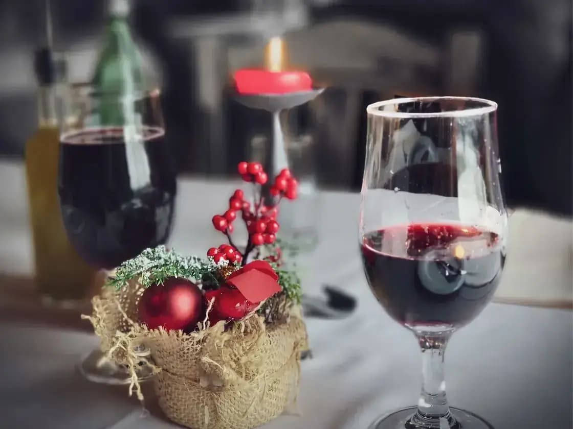 Two glasses of red wine on a restaurant table beside a small holiday arrangement