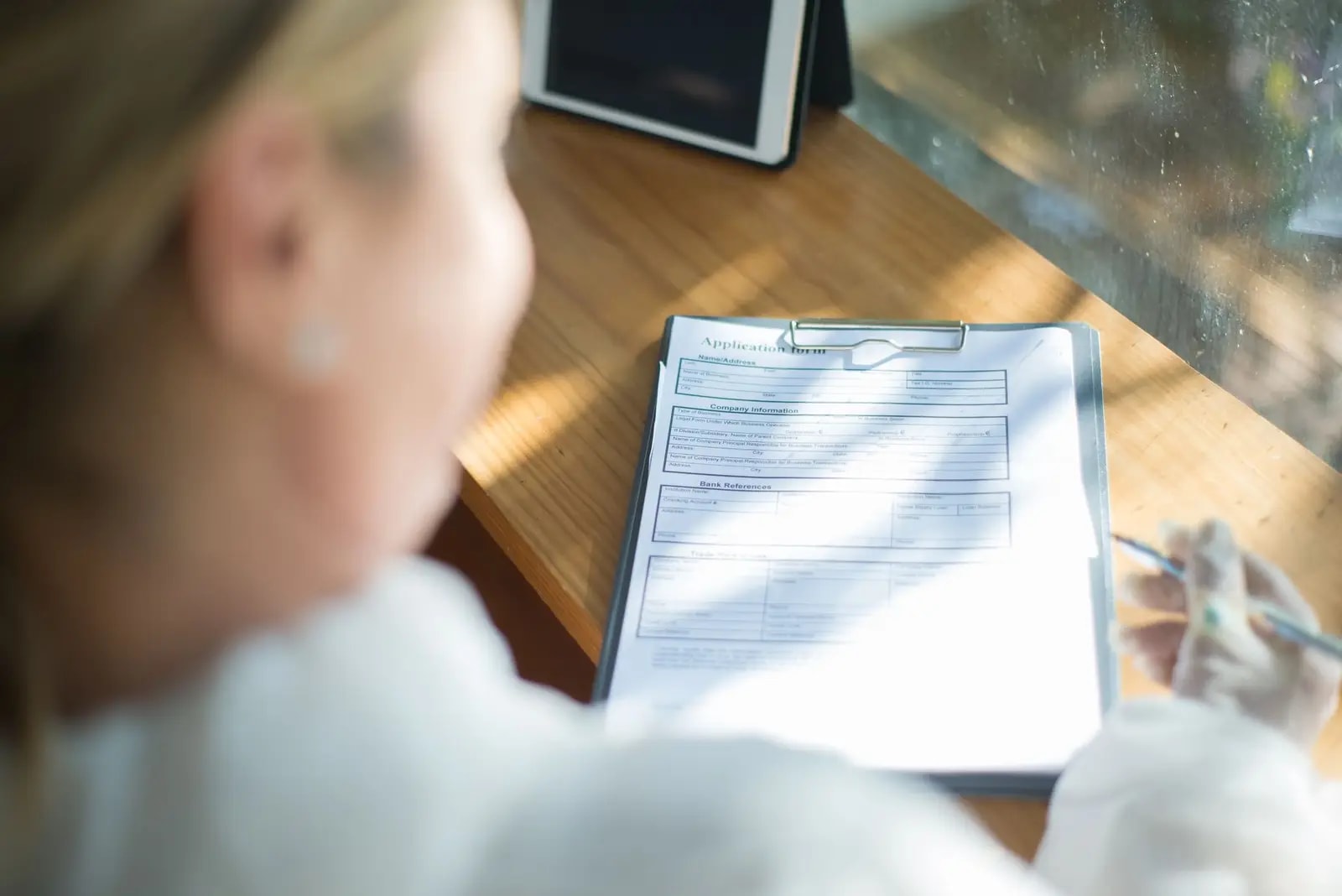 A person filling in a printed application form on a clipboard at a sunlit desk