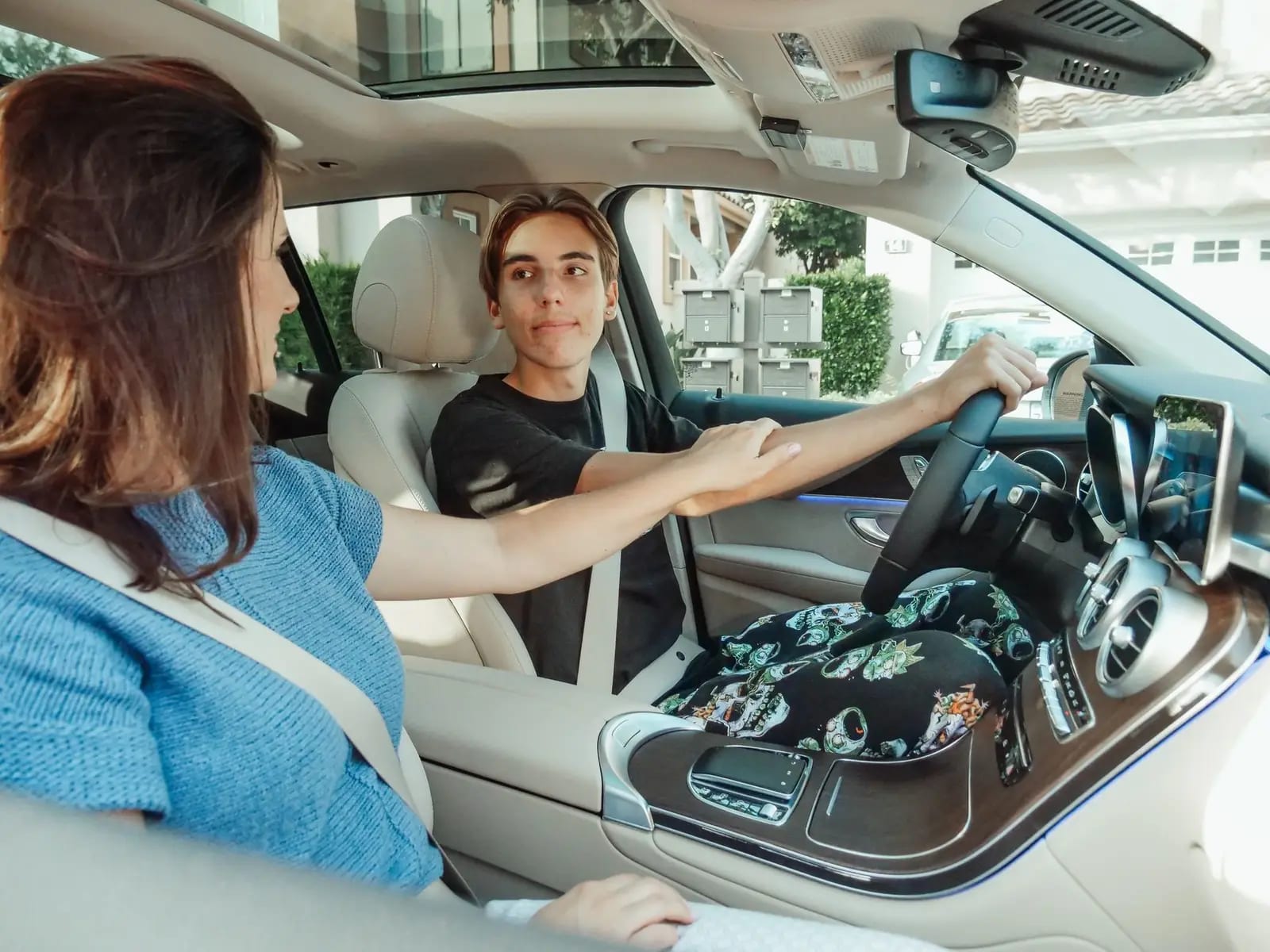 A young driver at the wheel of a parked car while an adult reaches across from the passenger seat