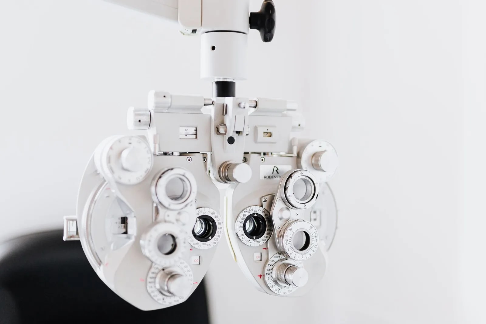 A white phoropter, the multi-lens instrument used to measure a glasses prescription, against a pale background