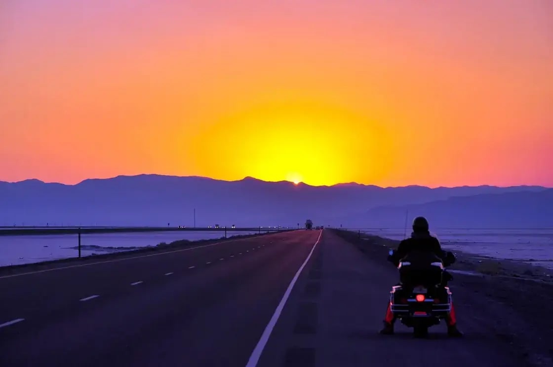 A lone figure on an empty highway at sunset with mountains ahead