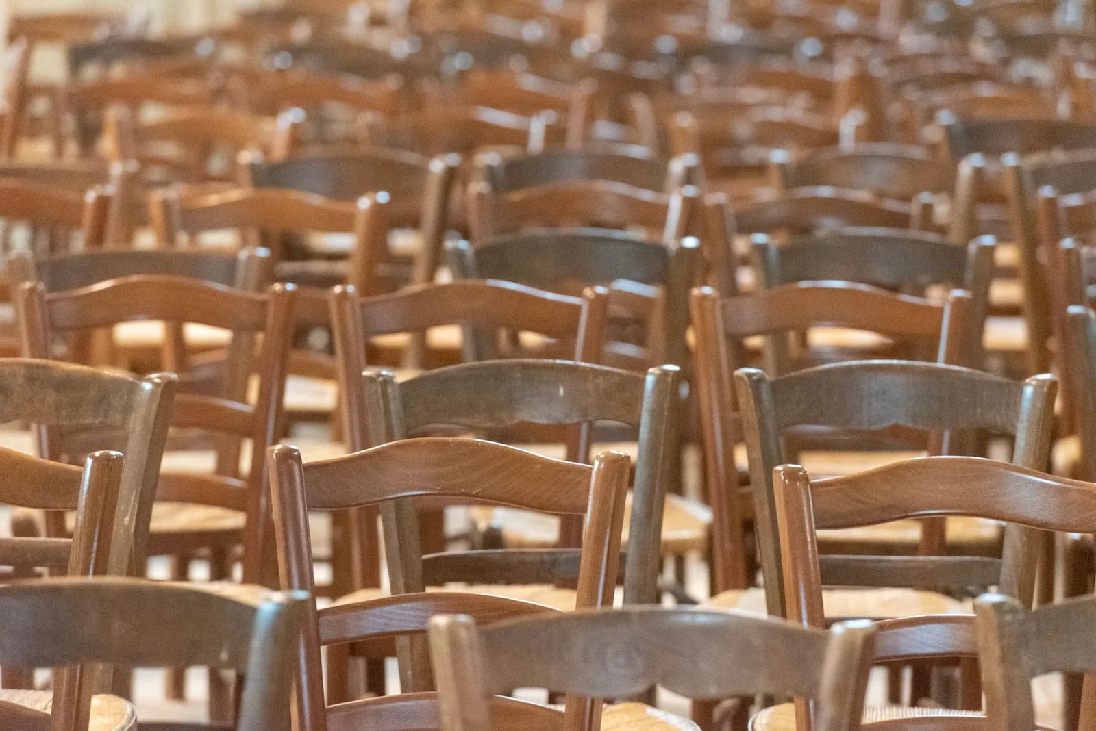 Rows of empty wooden rush-seated chairs set out in a hall