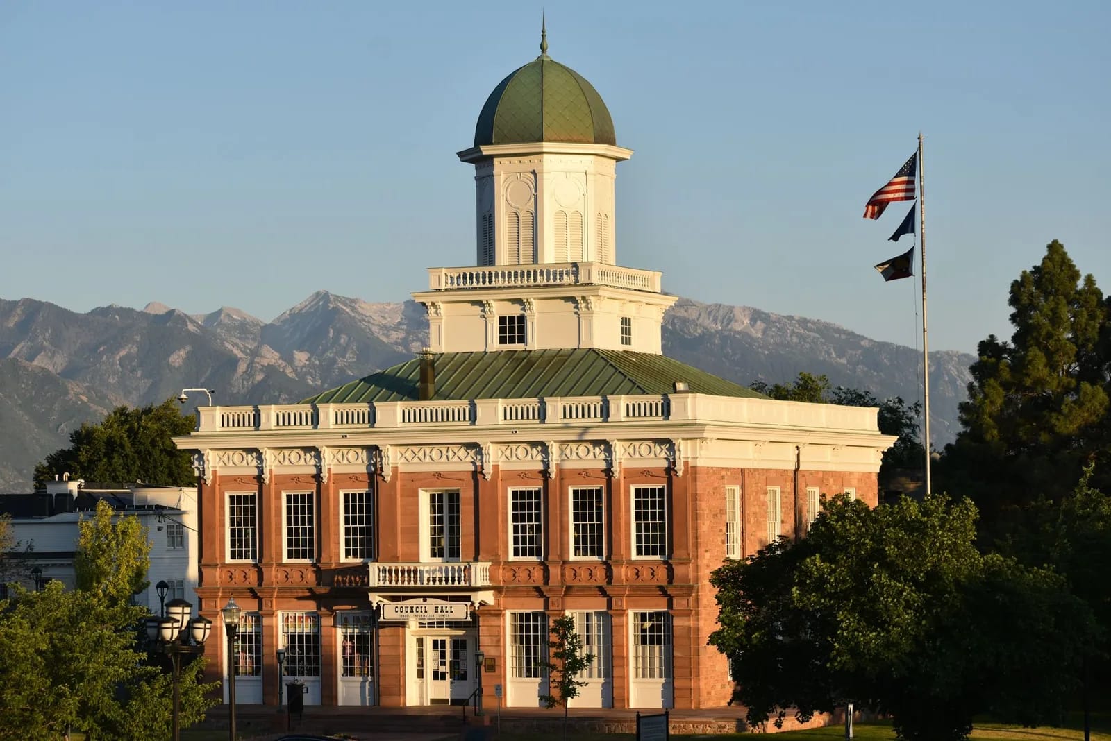 A historic civic hall with a domed cupola and a United States flag, mountains rising behind it