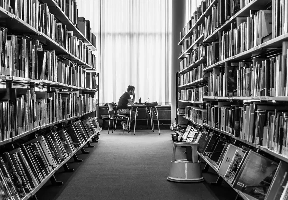 A student working at a desk between tall library shelves