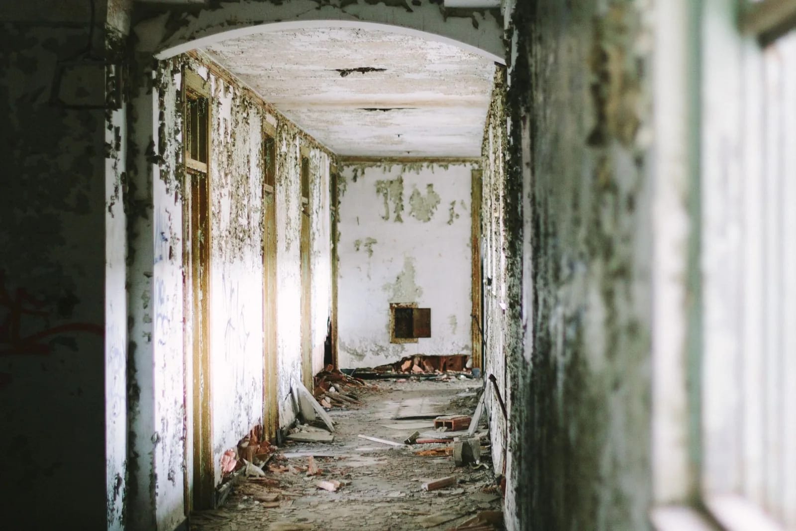 An abandoned corridor with peeling paint, exposed doorways and rubble scattered across the floor