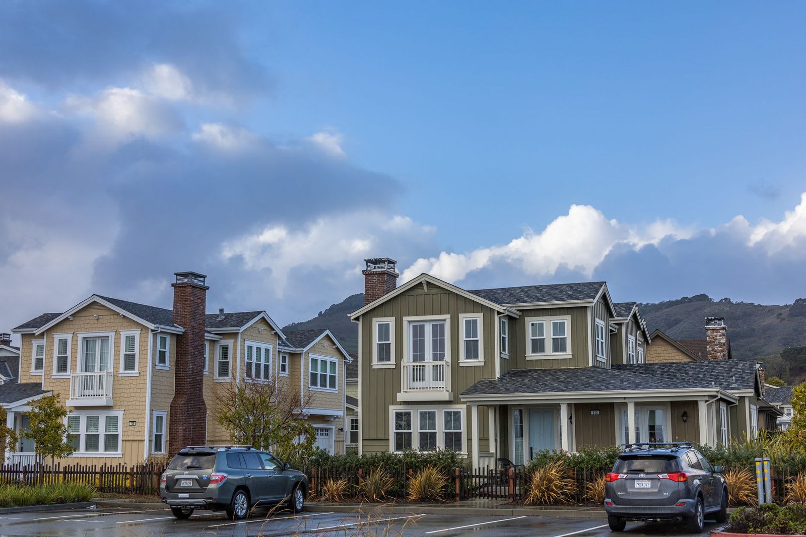 Two-story houses with front porches and brick chimneys along a street, with hills rising behind them