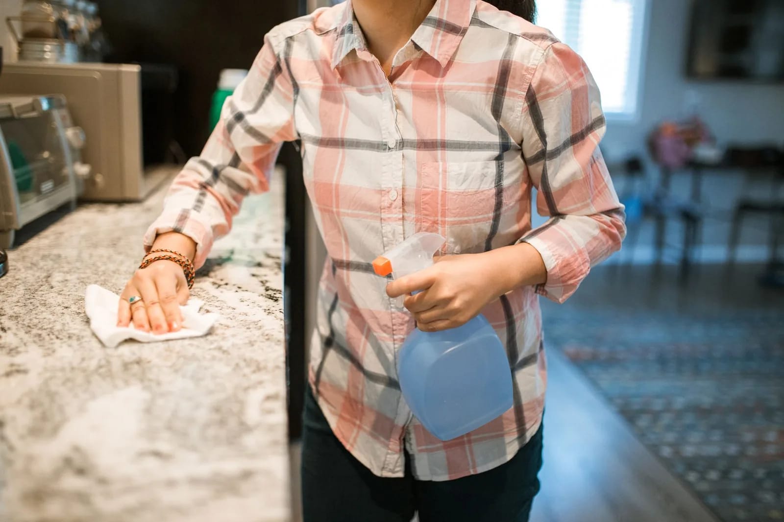 A person in a plaid shirt wiping a kitchen counter with a cloth and a spray bottle