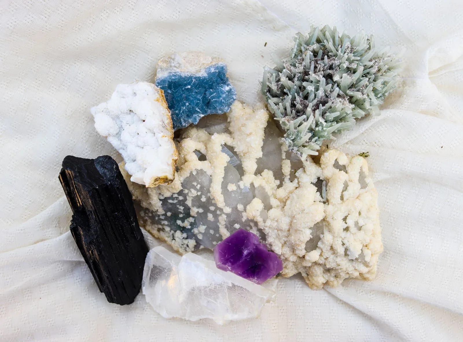 Mineral specimens including amethyst, clear quartz and black tourmaline arranged on pale cloth