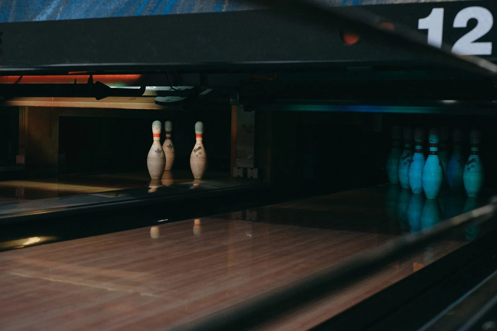 Bowling pins standing at the end of two dimly lit lanes, with the lane number 12 on the divider above