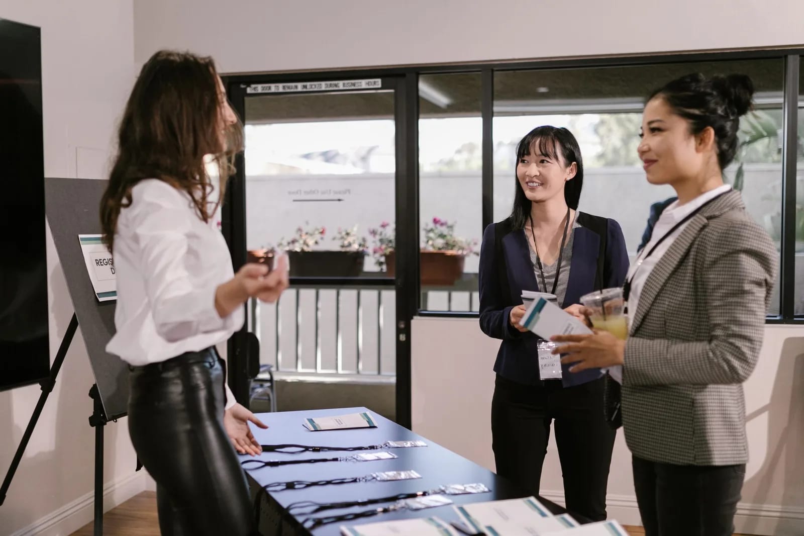 Two visitors wearing name badges talking with a staff member beside a check-in table laid out with lanyards