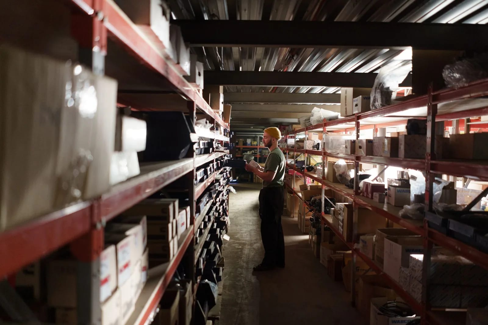 A worker walking a warehouse aisle lined with stocked shelving and boxes