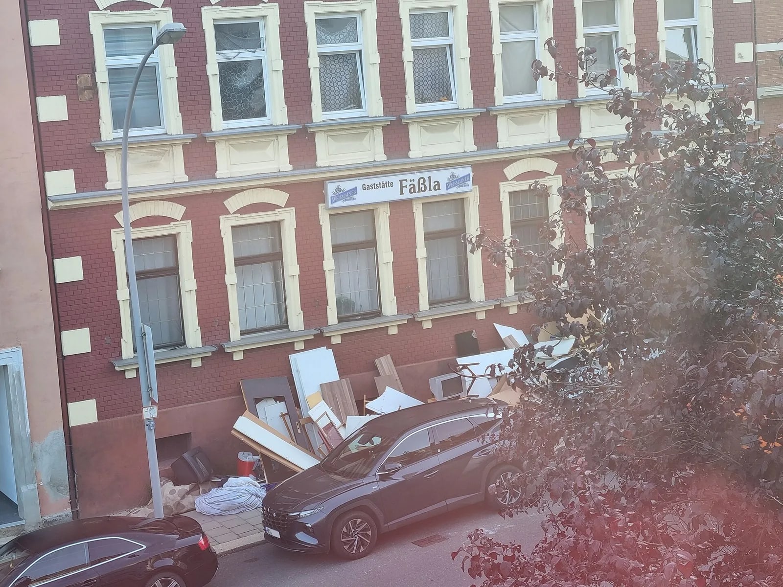 Discarded household furniture and bagged refuse piled on a pavement beside a building