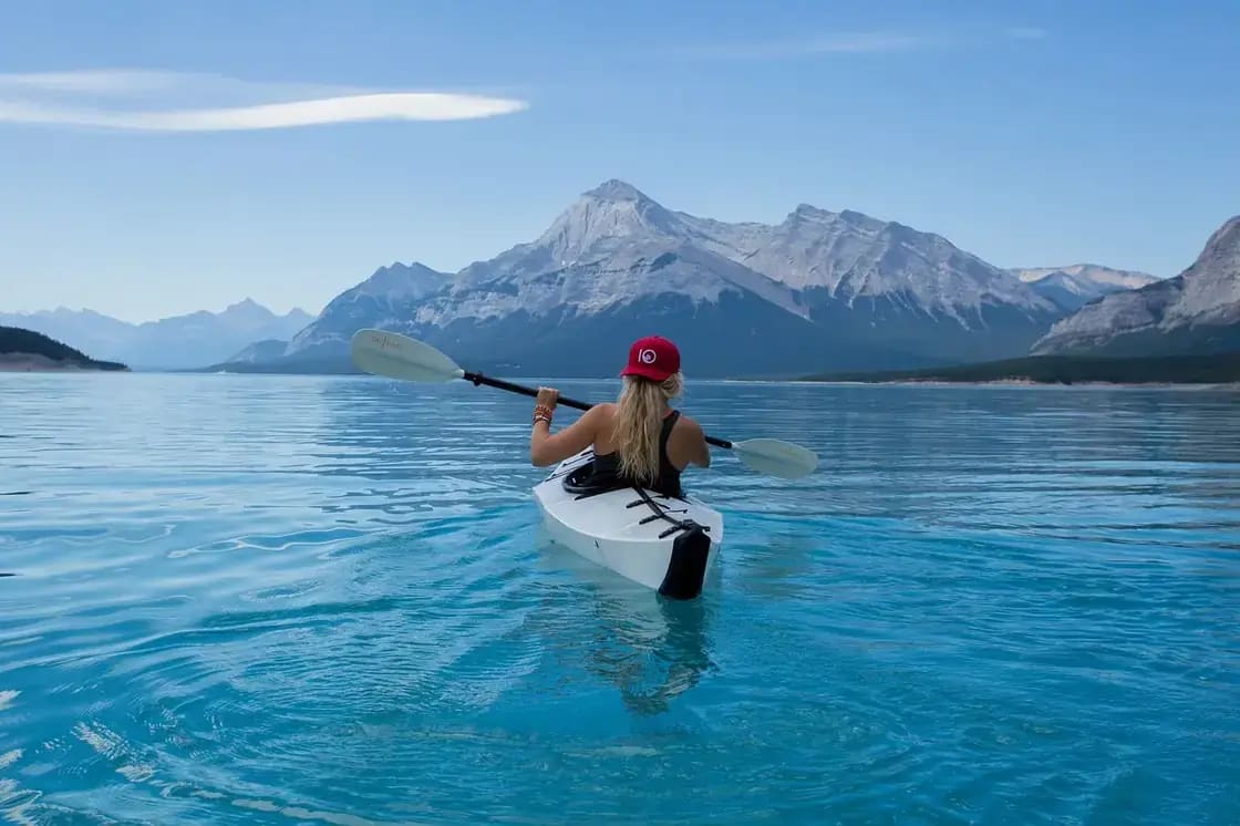 A kayaker paddling a calm mountain lake below snow-capped peaks