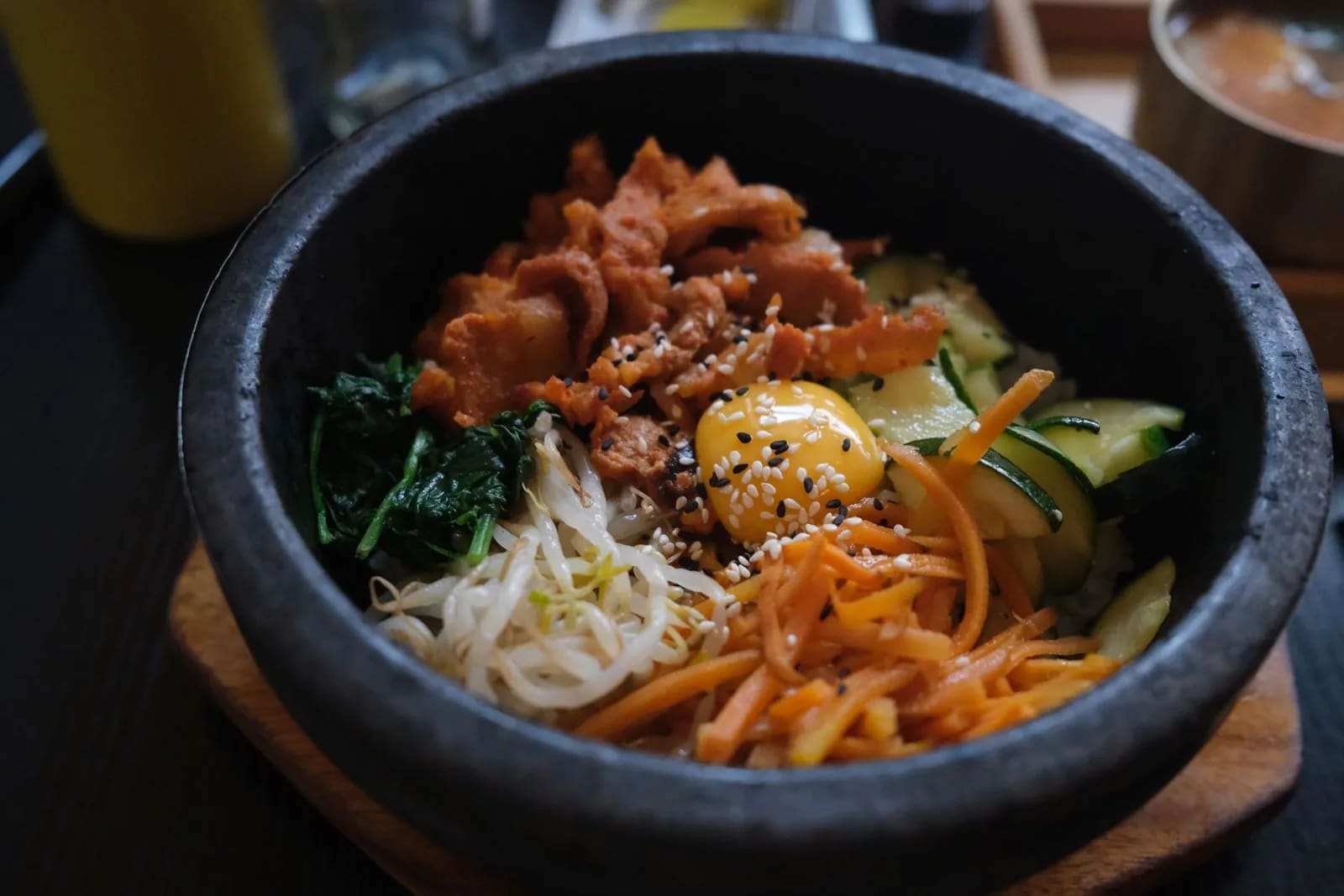 Korean bibimbap in a dark stone bowl where spicy pork and a raw egg yolk sit over rice with spinach, bean sprouts and shredded carrot