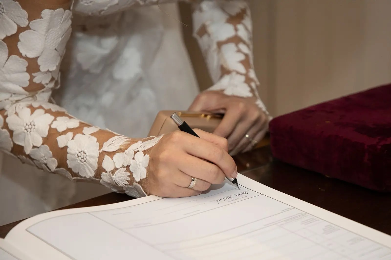 A bride in a lace-sleeved dress signing a marriage register at a table