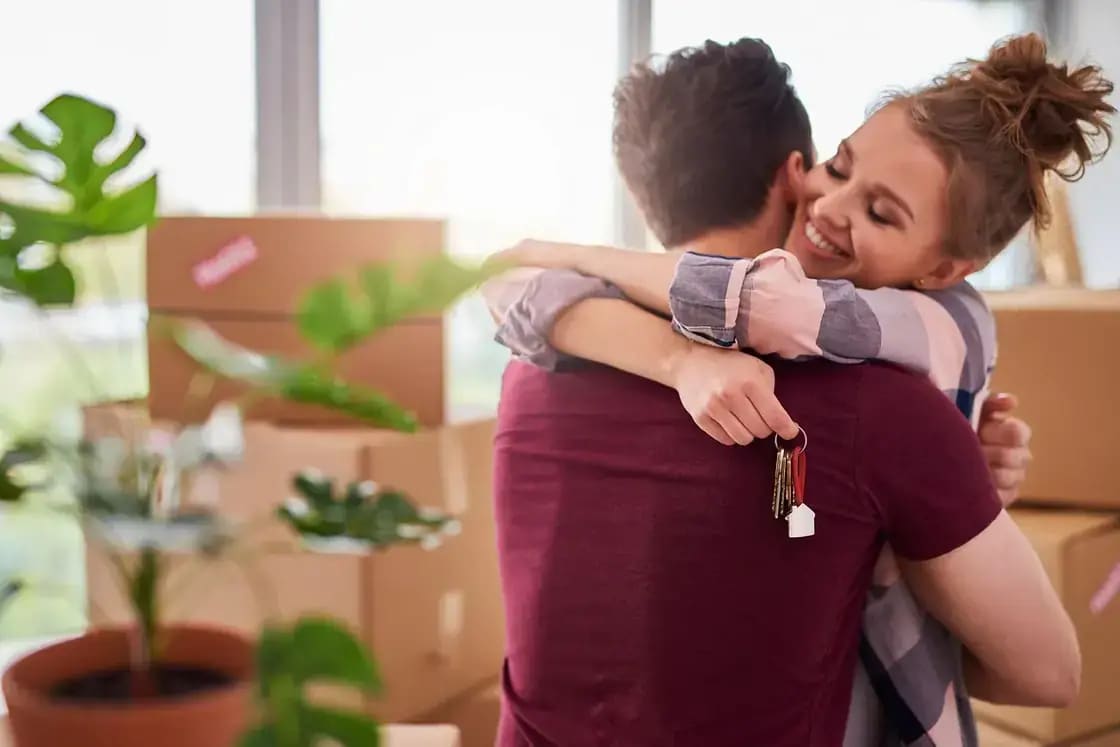A couple embracing among moving boxes, holding a set of keys