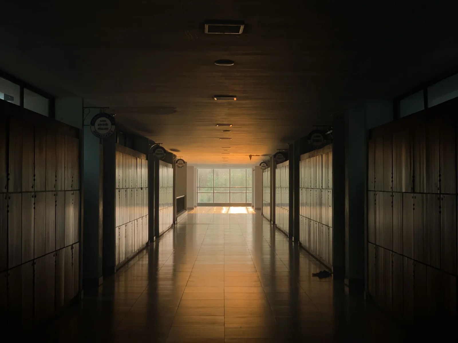 A dim school corridor lined with lockers, with daylight at the far end