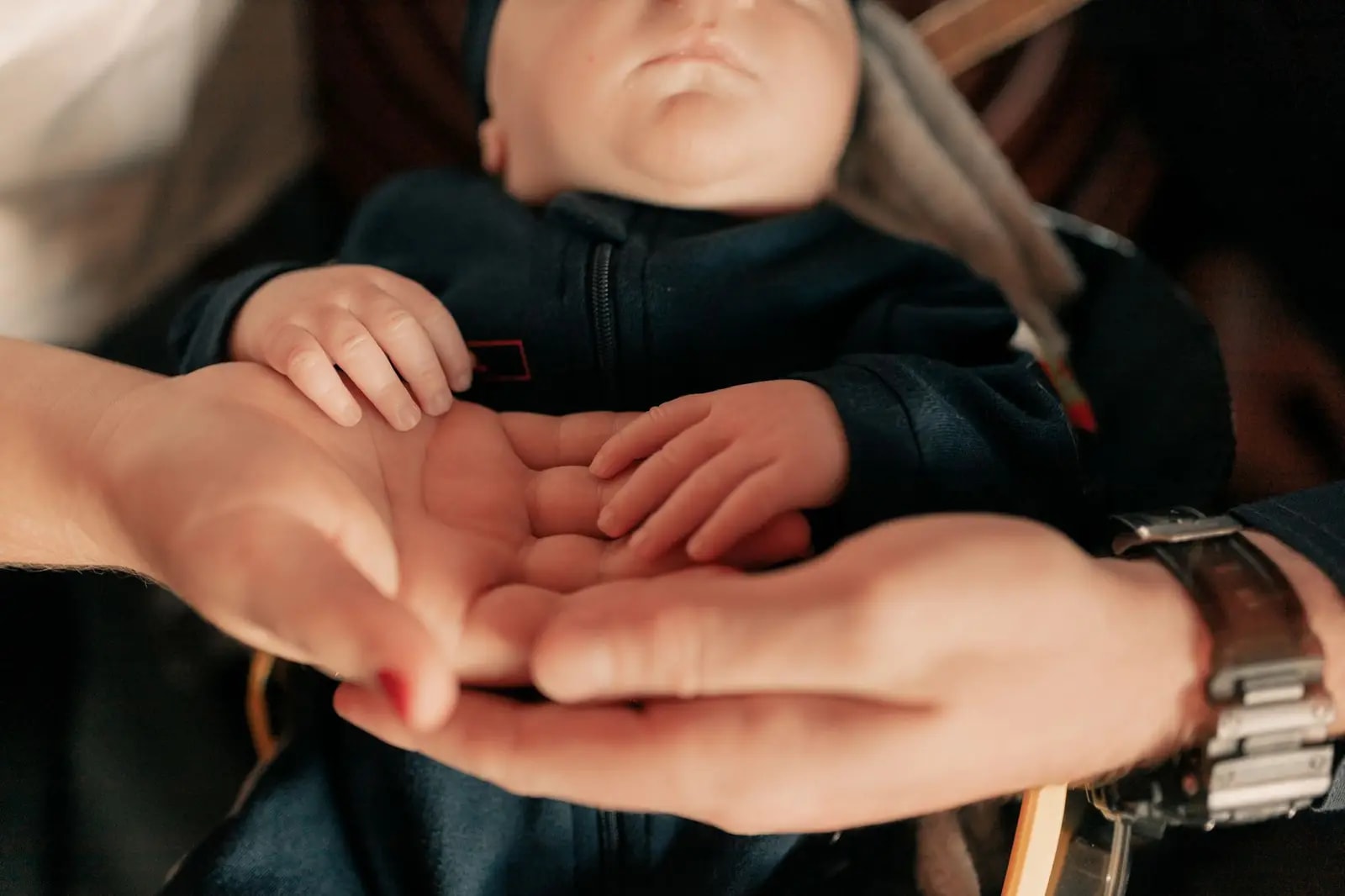 Close-up of parents holding their baby's hands, symbolizing love and protection