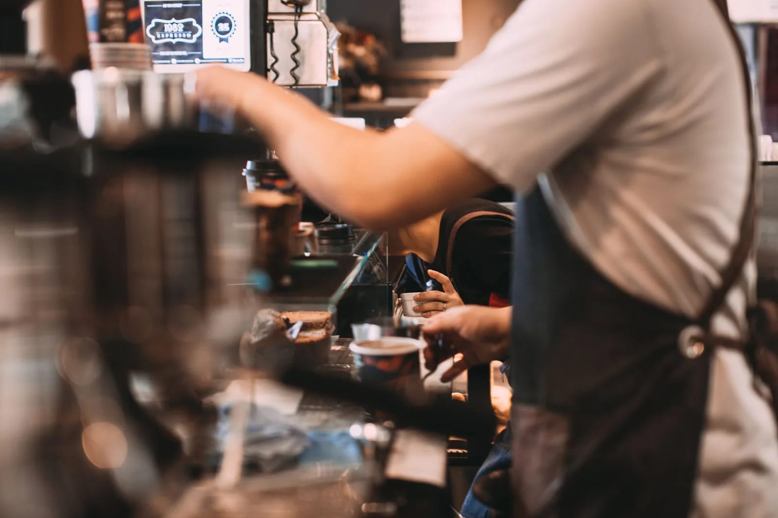 A barista in an apron preparing drinks behind a busy cafe counter