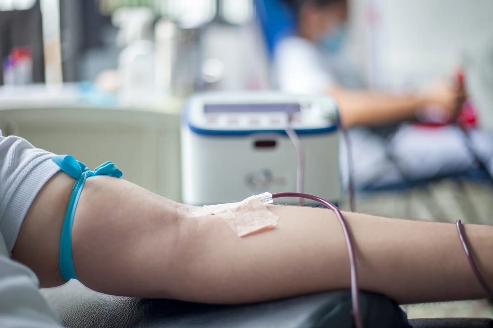 A forearm with a tourniquet and taped cannula, tubing running to a collection machine