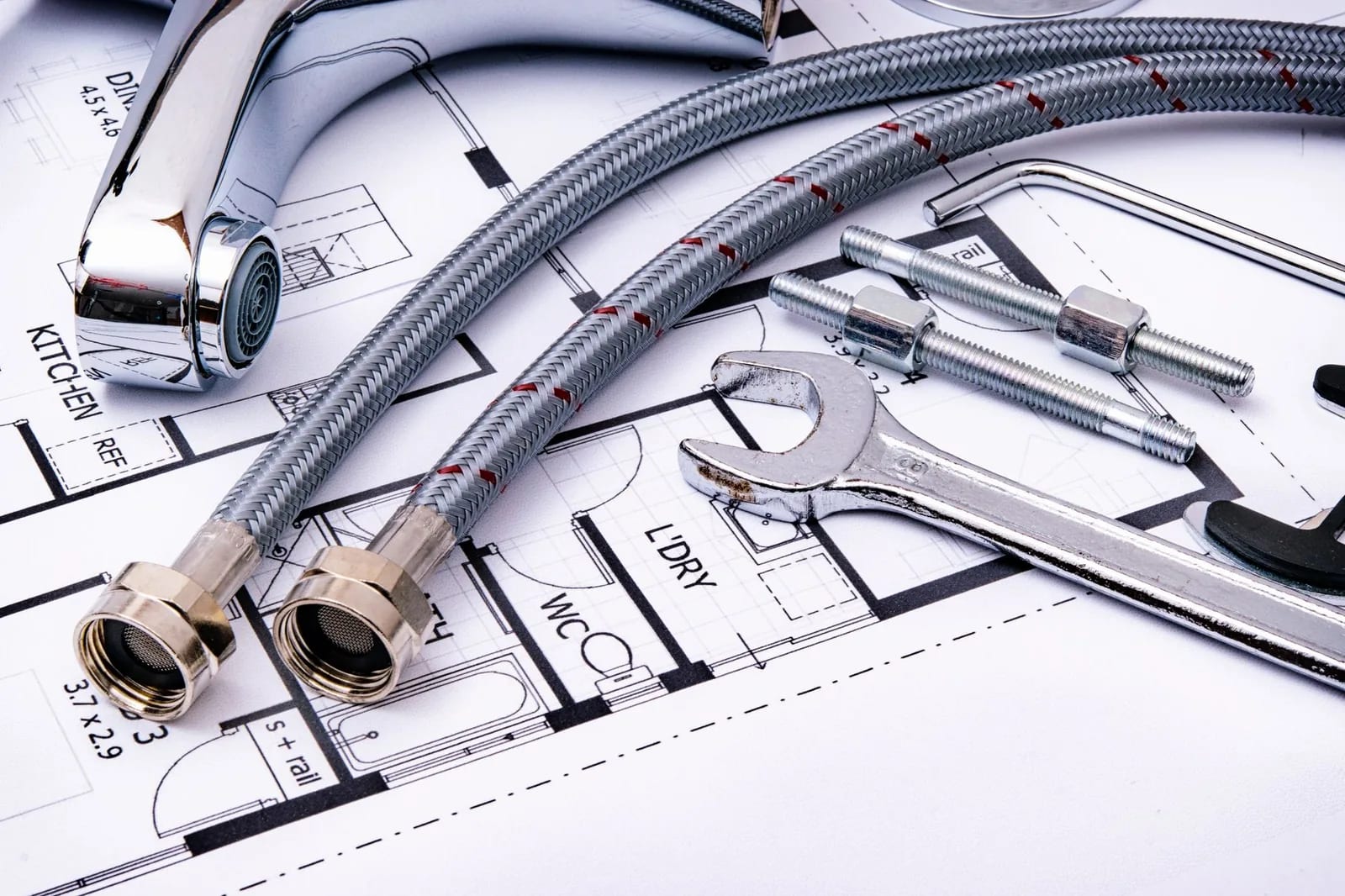 A faucet, braided supply hoses and a wrench laid out on a kitchen and bathroom floor plan