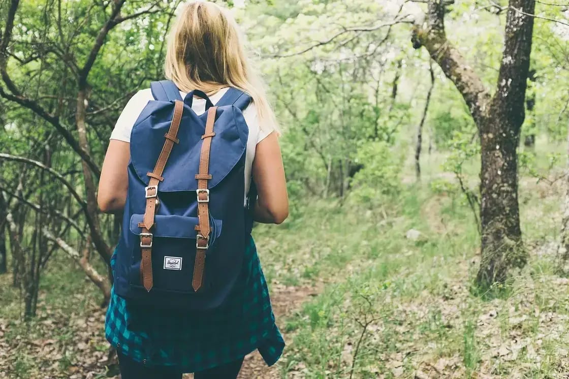 A woman with a backpack walking a wooded trail